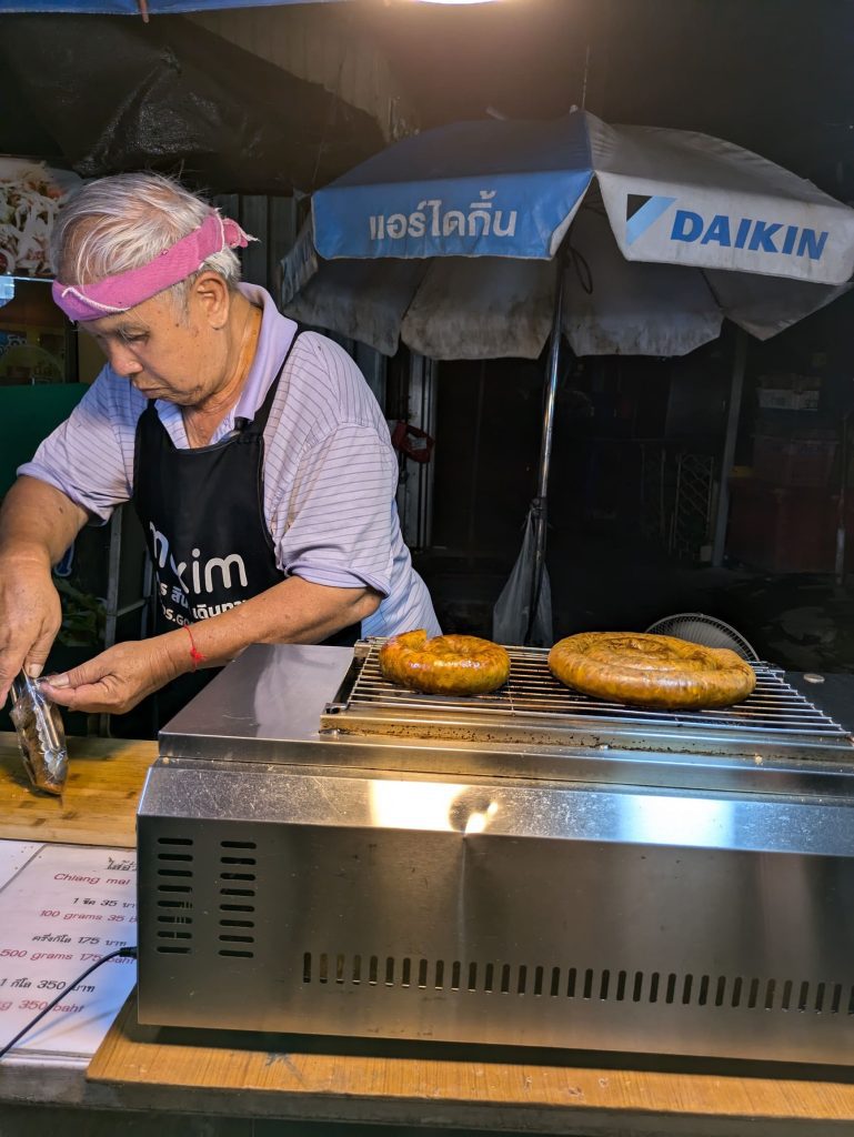 Un hombre corta un trozo de salchicha Sai Oua, típica de Chiang Mai, en un mercado callejero nocturno